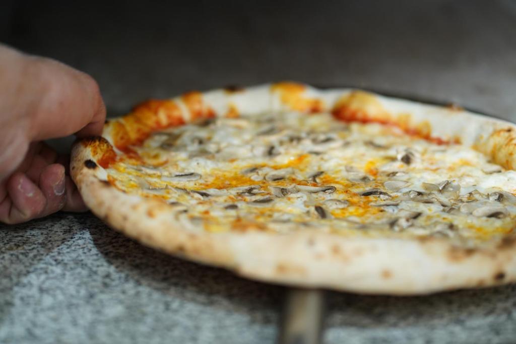 Pica ar sēnēm tiek izņemta no krāsns, uzsverot tās zeltaini brūno garoza un izsalkumu rosinošo izskatu.