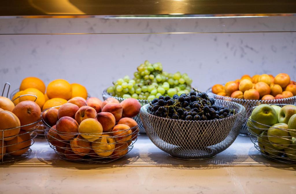 Svaigu augļu izlase dažādās grozā, tostarp apelsīni, vīnogas, persiki un āboli.