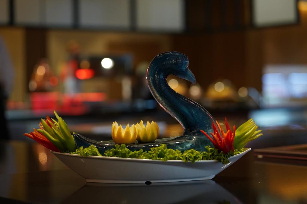 Skaista dekorācija ar putnu formu, izgatavota no dārzeņiem un augļiem, novietota uz galda, apstādīta ar zaļumiem.