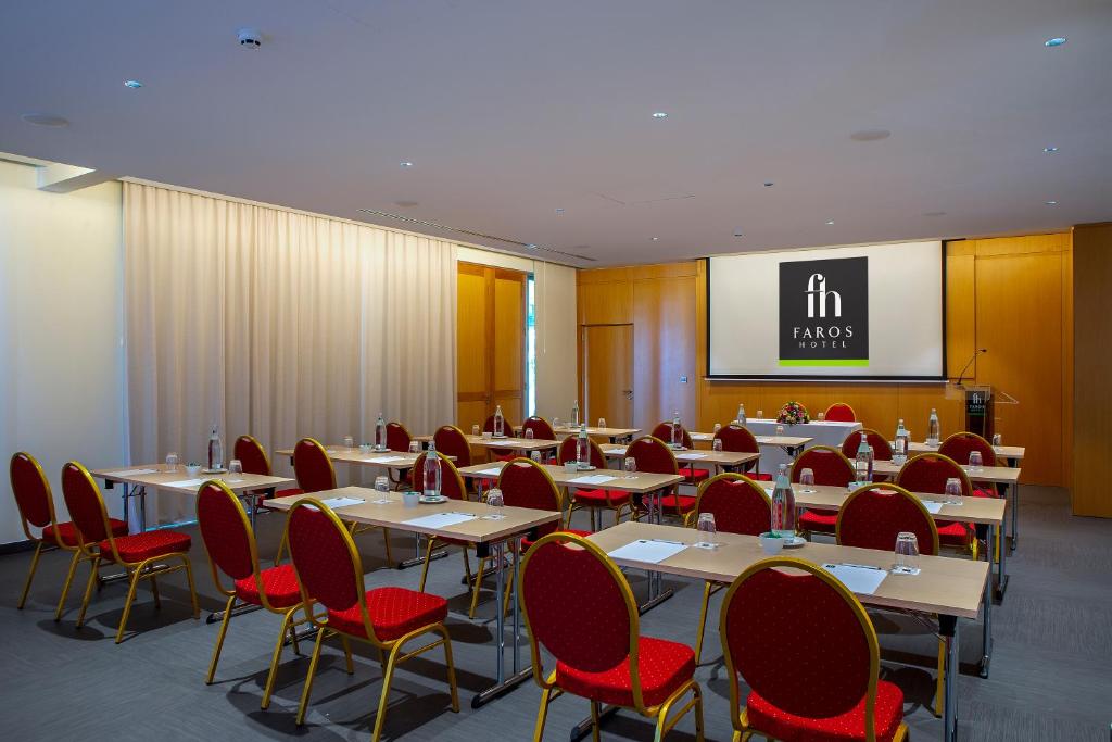Konferences telpa ar sarkaniem krēsliem un galds, kas sagatavots sanāksmei, ar "Faros Hotel" logo ekrānā.
