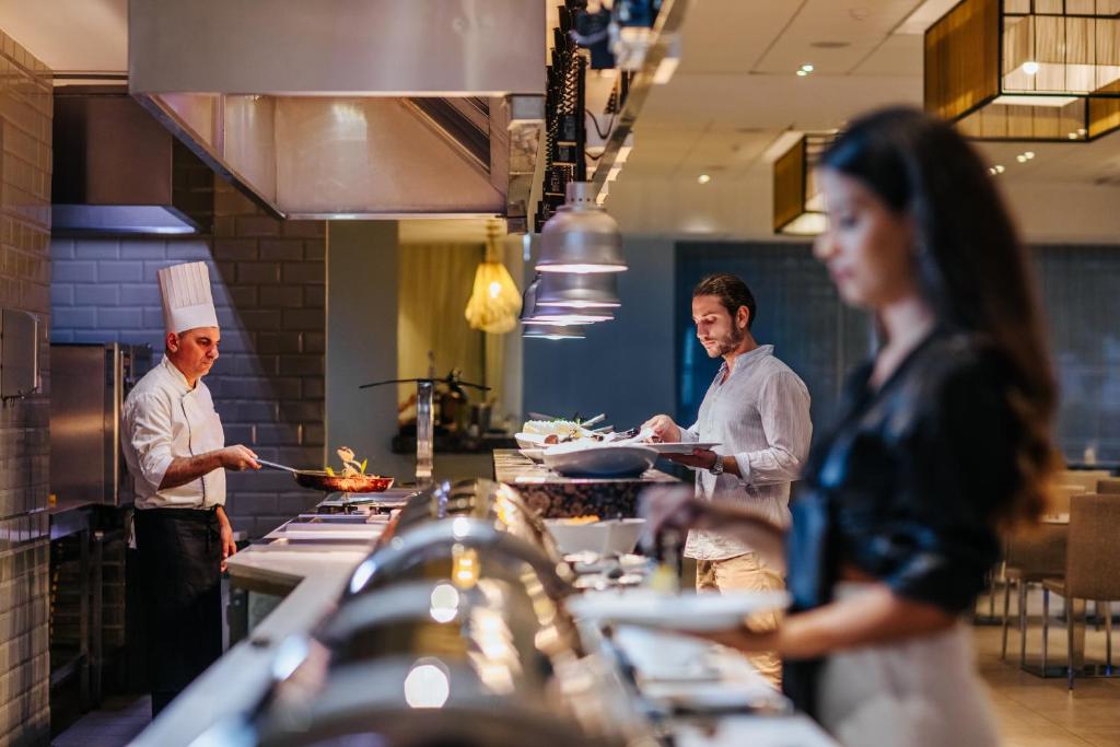 Atsvaidzinoša aina mūsdienīgā restorānā, kur šefpavārs gatavo ēdienus, kamēr viesi izvēlas maltīti no bufetes galda.