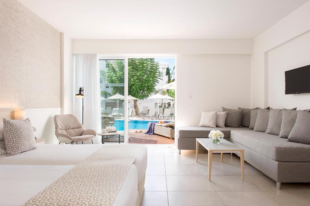 Mūsdienīga viesnīcas numura iekšskats ar ērtu gultu, dīvānu un skatu uz baseinu. Telpa ir gaiša un minimālistiska, radot relaksējošu atmosfēru.