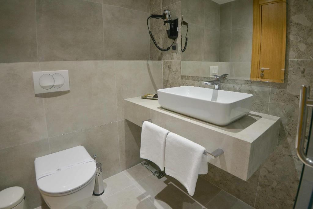 Moderns vannas istabas dizains ar pelēku flīžu apdari, elegantu izlietni un higiēnas ierīcēm. Iekļauti arī dvieļu turētājs un spogulis.