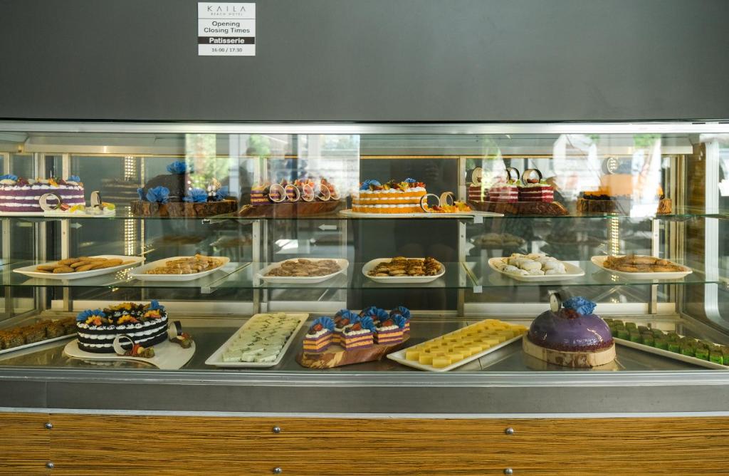 Deserts un kūkas vitrīnā ar dažādiem krāsainiem un dekorētiem saldumiem. Rūpīgi sakārtoti izstrādājumi, tostarp kūkas, cepumi un konfektes, kas vilina ar savu izskatu.