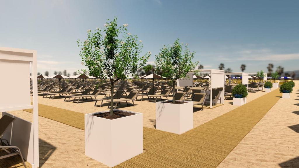 Pludmales atpūtas zona ar saulessargiem un guļamkrēslām, dekorēta ar augiem un kokiem. Ceļš no koka dēļiem ved cauri smiltīm, radot mierīgu un relaksējošu atmosfēru.