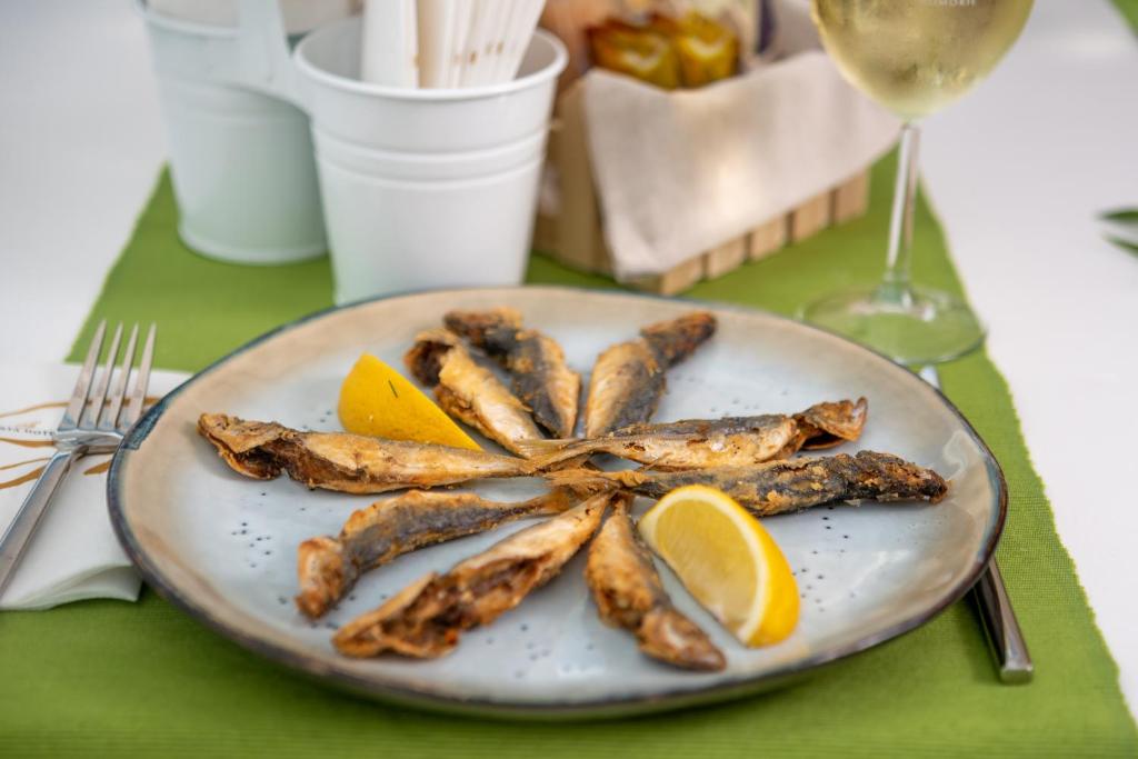 Fried fish arranged in a circular pattern on a plate, garnished with lemon slices, served with a glass of white wine.