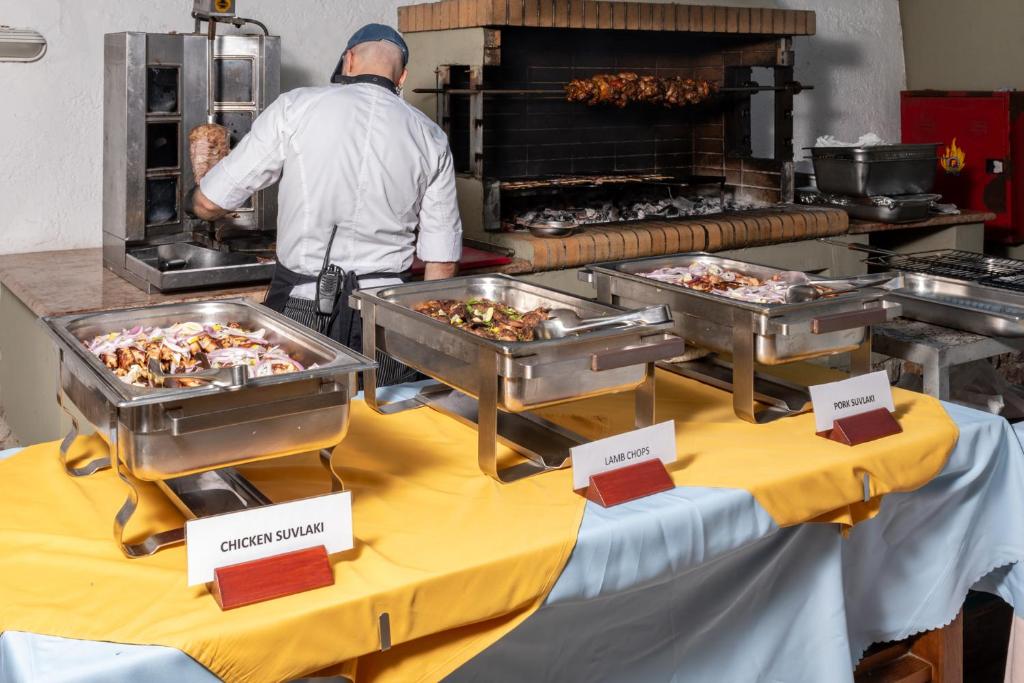 Bārs ar dažādiem grilētiem ēdieniem, tostarp vistas suvlaki, jēra karbonādes un cūkgaļas suvlaki, kamēr šefpavārs strādā pie grila.
