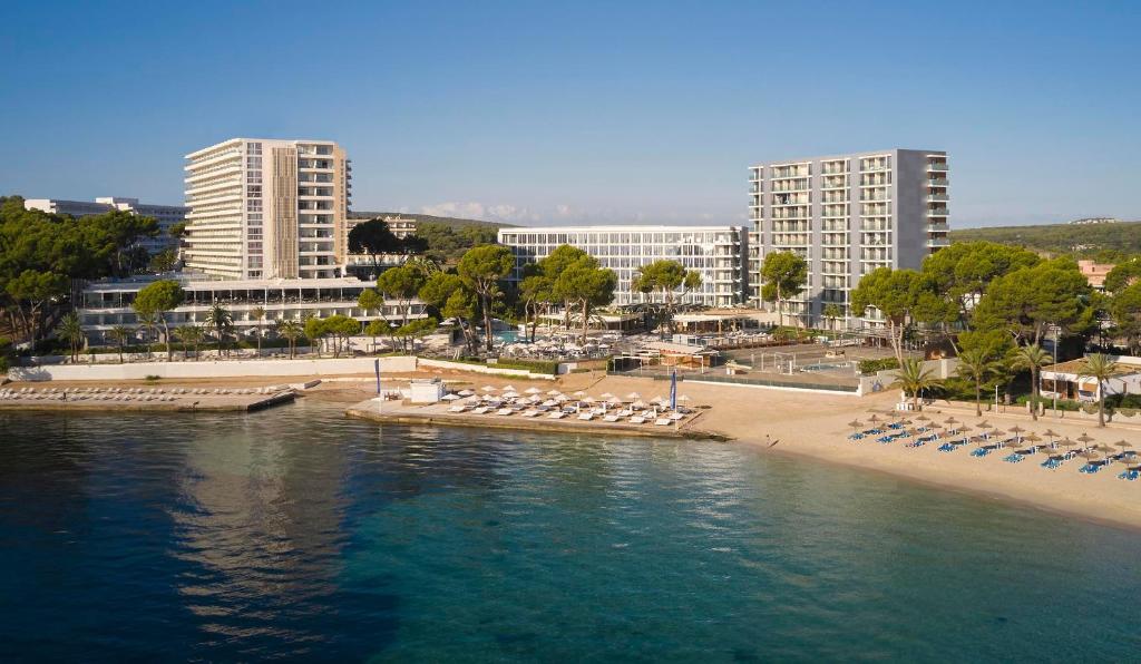 Mūsdienīgs kūrorts pie pludmales ar ēkām un palmām, kas atspoguļo relaksējošu atmosfēru. Skaists skats uz ūdeni un sauļošanās krēsliem pludmalē.