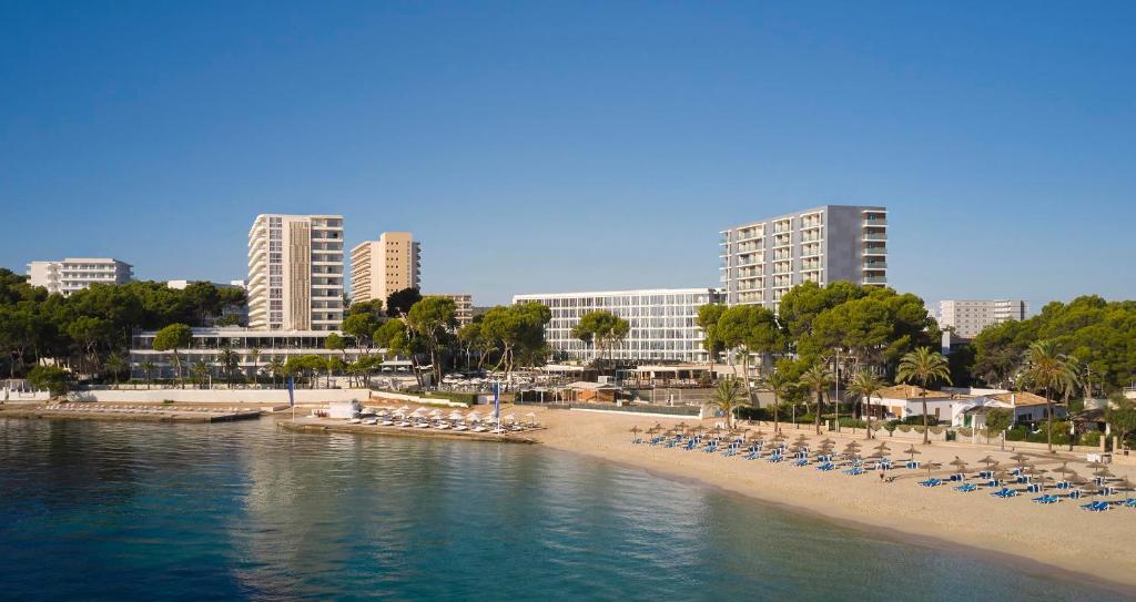 Mūsdienīgs pludmales kūrorts ar viesnīcām, kas atrodas pie saulainas pludmales, kurā ir saulessargi un atpūtas krēsli. Tīrs ūdens un zaļi koki veido relaksējošu atmosfēru.