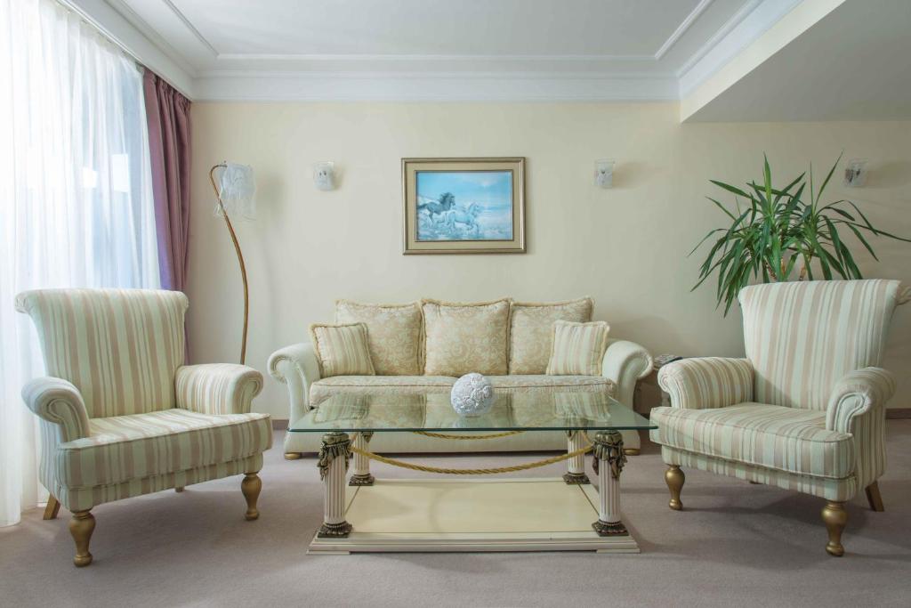 Mūsdienīgs viesistabas interjers ar diviem ērtiem krēsliem un dīvānu, kas novietots pie stikla galda. Sienā ir glezna ar ainavu un redzams zaļš augs.