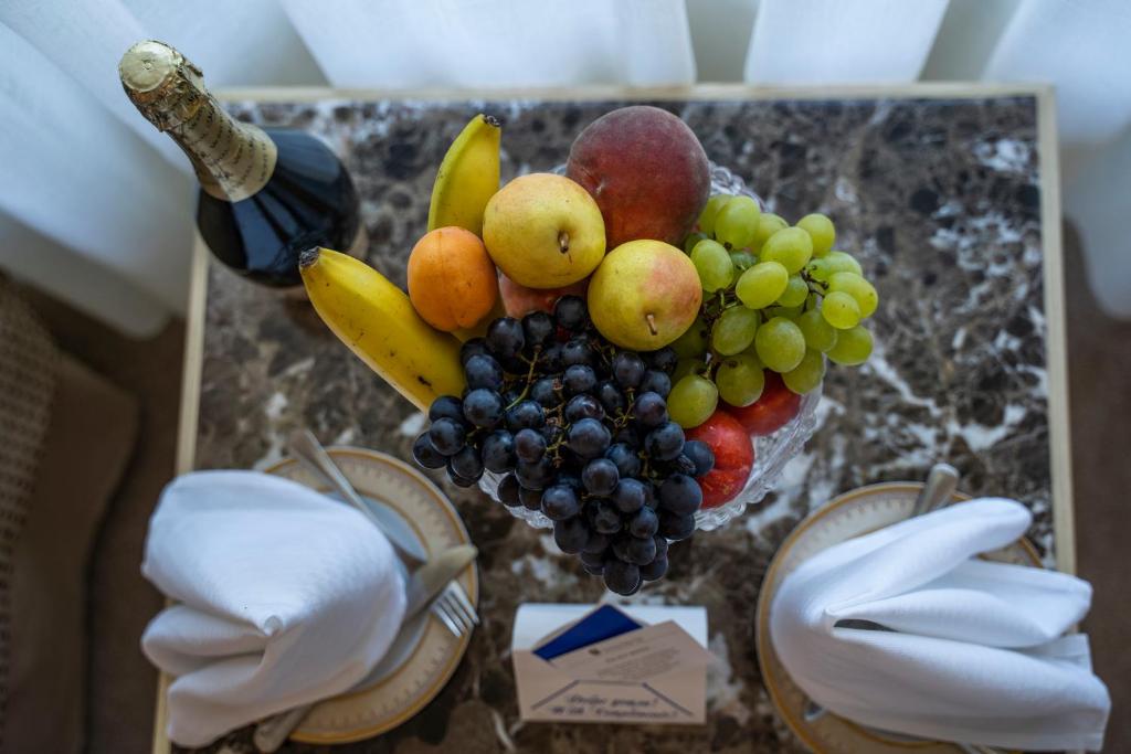 Augļu kompozīcija ar vīnu, kas novietota uz marmora galda. Uz galda redzami dažādi augļi, kā banāni, vīnogas, āboli un bumbieri, kā arī salvetes un galda piederumi.