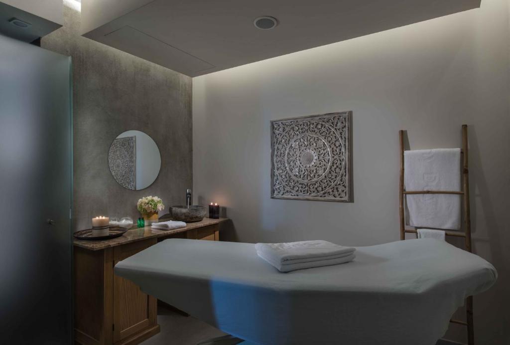 Relaksējošs spa telpas interjers ar masāžas galdu, dekoratīvu sienu un sveču apgaismojumu. Telpa ir aprīkota ar ziediem un dvieļiem, radot mierīgu atmosfēru.