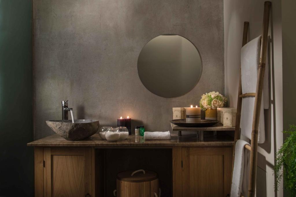 Mūsdienīgs vannas istabas interjers ar akmens izlietni, apaļu spoguli un svecēm, radot relaksējošu atmosfēru. Dabiski materiāli un dekoratīvi elementu kombinācija.