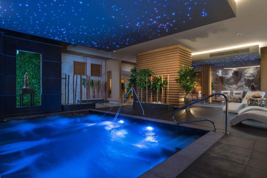 Mūsdienīgs spa ar zilu apgaismojumu un relaksējošu atmosfēru, kurā redzama burbuļvanna, zaļumi un stilīgas atpūtas zonas. Ideāls vieta atpūtai un relaksācijai.