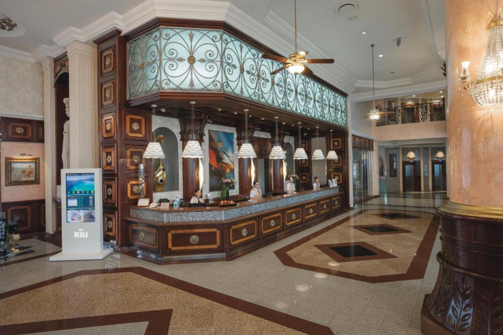 Luksusa viesnīcas reģistratūra ar elegantu apdari un mūsdienīgu tehnoloģiju, kur darbinieki apkalpo viesus. Gaismas un mākslas elementi rada siltu un viesmīlīgu atmosfēru.