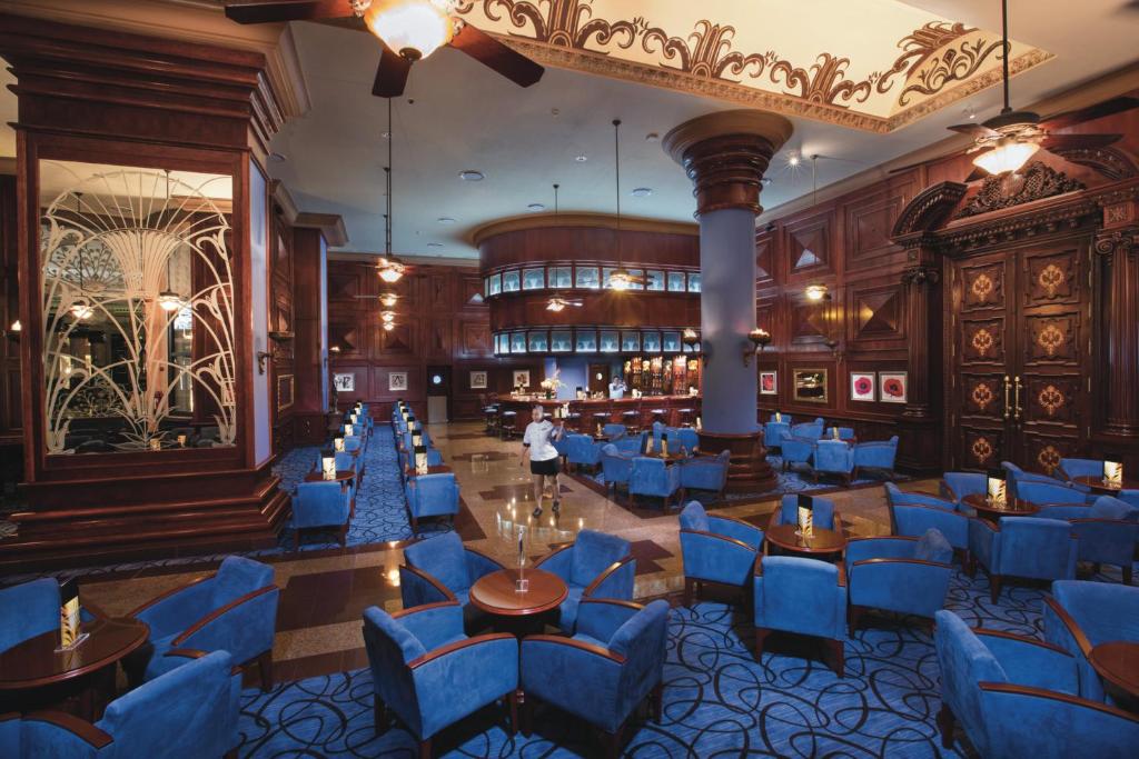 Elegants bārs ar zilu krēslu un koka interjeru, kas piedāvā komfortablu vidi relaksācijai. Izcila apgaismojuma un dekorāciju kombinācija rada patīkamu atmosfēru.