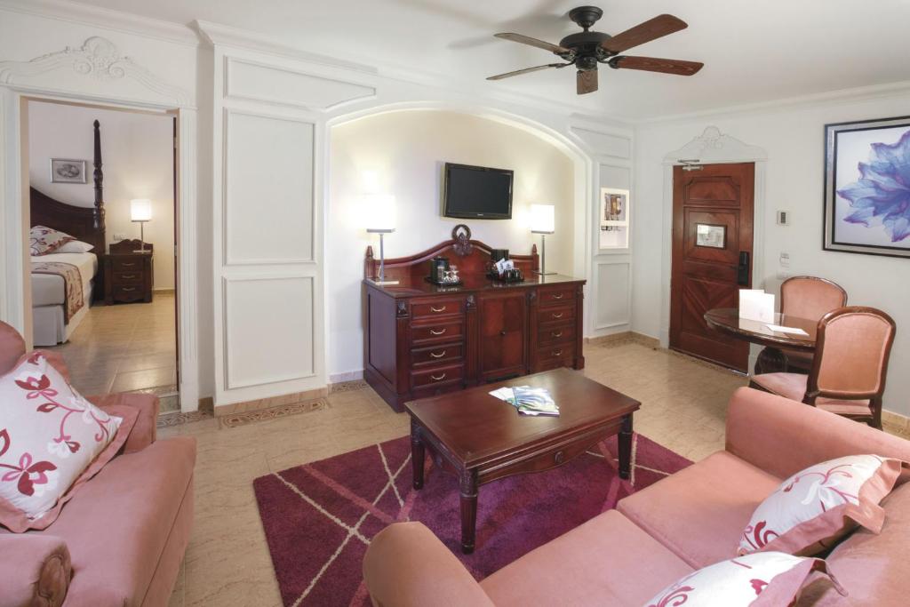 Eleganta viesnīcas numura interjers ar mēbelēm, kas izgatavotas no tumša koka, un komfortablu sēdvietu zonu. Gaismas elementi un dekoratīvie akcenti piešķir siltumu un mājīgumu telpai.