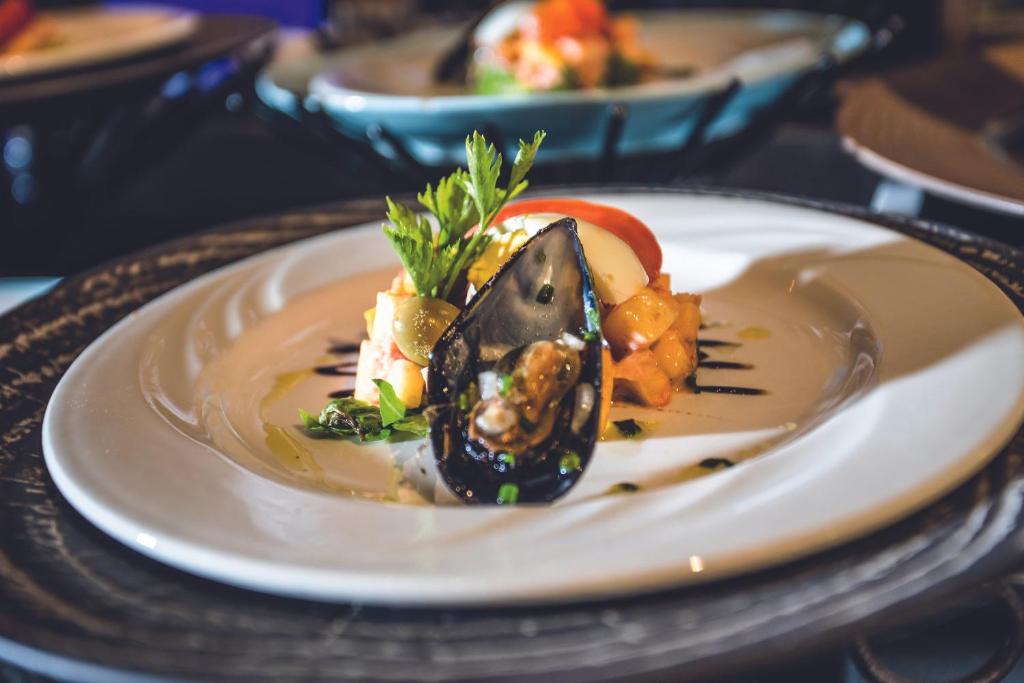 Elegantā šķīvī pasniegts jūras velšu ēdiens ar melnā čaula mizi un dārzeņu garnējumu, pievienots svaigs pētersīlis.