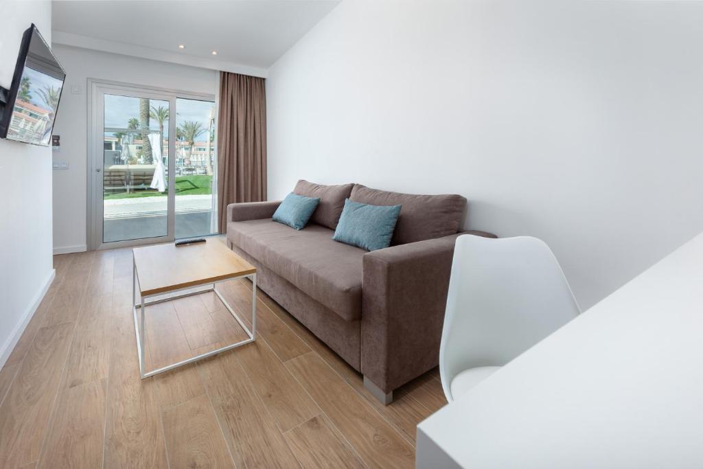 Mūsdienīga viesistaba ar brūnu dīvānu, baltu krēslu un stikla galdu, kas piedāvā skatu uz terasi un dārzu. Telpā ir gaišas sienas un koka grīdas.