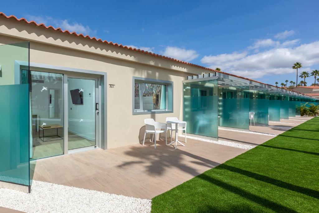 Mūsdienīgs viesnīcas numurs ar stikla sienām un terasi, kas piedāvā relaksējošu skatu uz zaļu zāli un palmām. Ideāls brīvdienu galamērķis saulainā vidē.