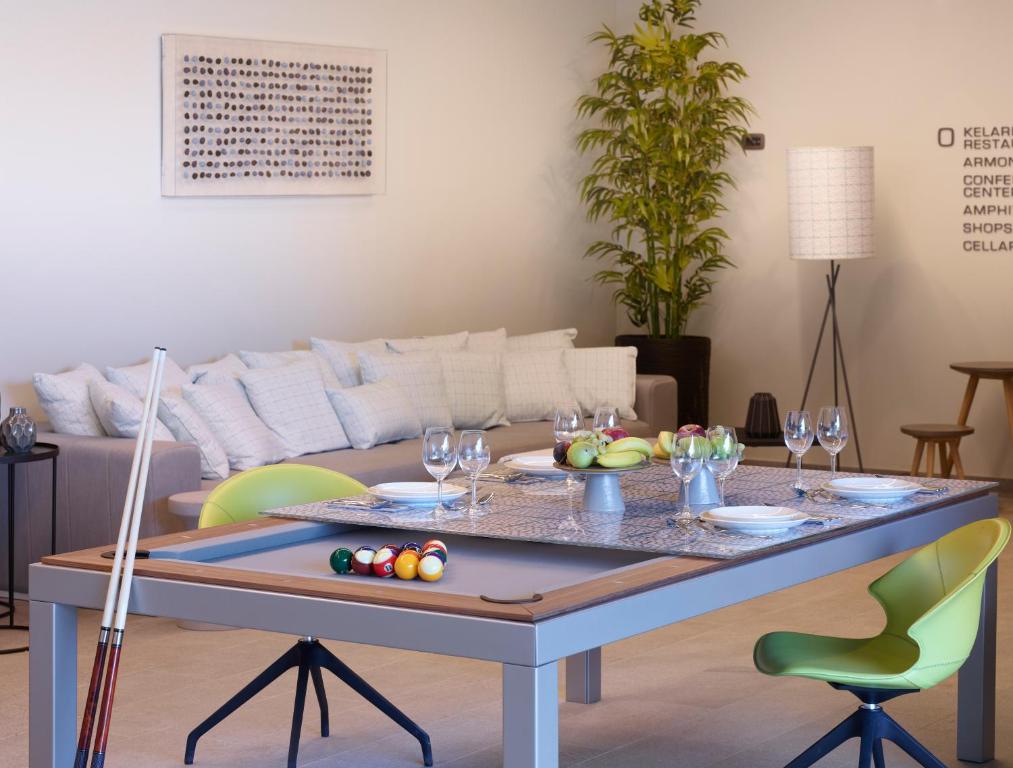 Mūsdienīgs dzīvojamās istabas interjers ar biljarda galdu, elegantu apgaismojumu un augu akcentiem. Uz galda ir izkārtoti trauki un augļi, radot viesmīlīgu atmosfēru.