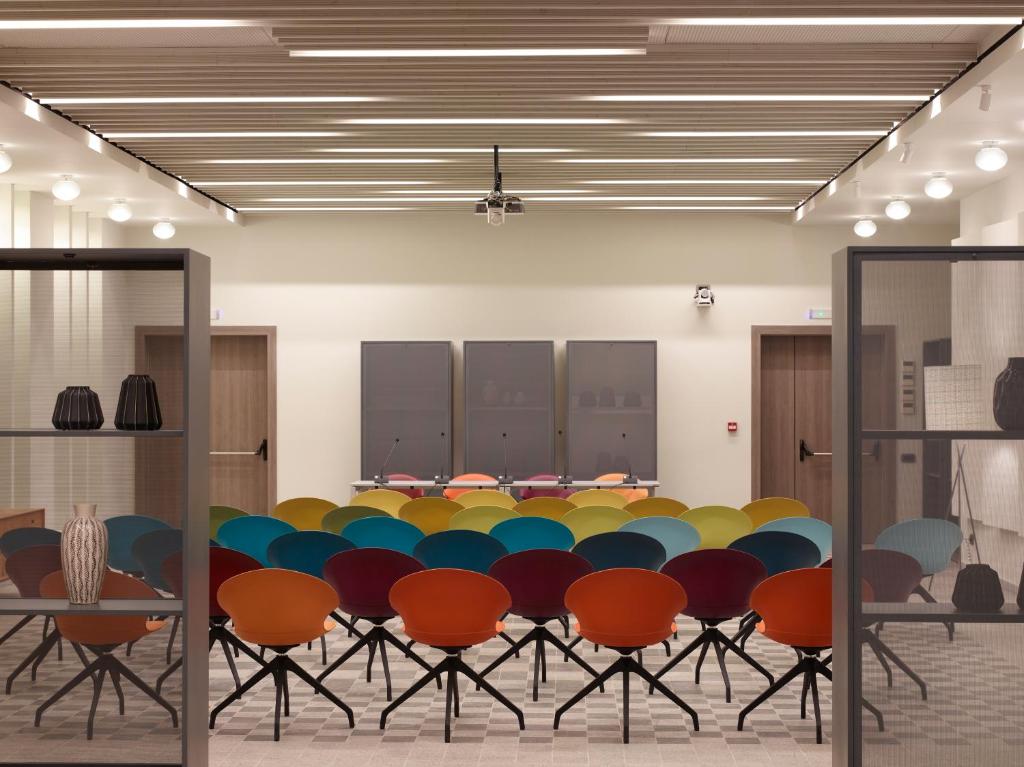 Mūsdienīga sanāksmju telpa ar krāsainām krēslām un lielu skatu uz priekšējo daļu. Telpā ir labi apgaismojums un stilīgs interjers.