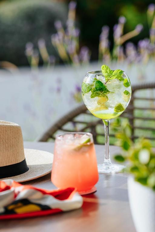 Vasaras dzērieni uz galda, ar gāzētu kokteili un augļu dzērienu, fonā ziedi un saulains laiks.