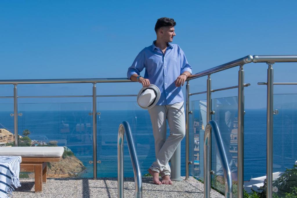 Jauns vīrietis atpūšas uz terases pie Blue Bay Resort Crete, ar skatu uz jūru.