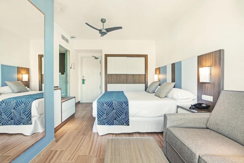 Mūsdienīga viesnīcas istaba ar divguļamo gultu, dīvānu un elegantu apgaismojumu, radot komfortablu un relaksējošu atmosfēru.