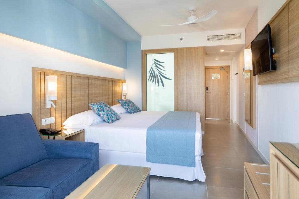 Mūsdienīgs viesnīcas numurs ar divguļamo gultu, dīvānu un modernu interjeru, kas ietver gaišas krāsas un koka akcentus. Numurā ir televizors un liels logs ar dekoratīvu stiklu.