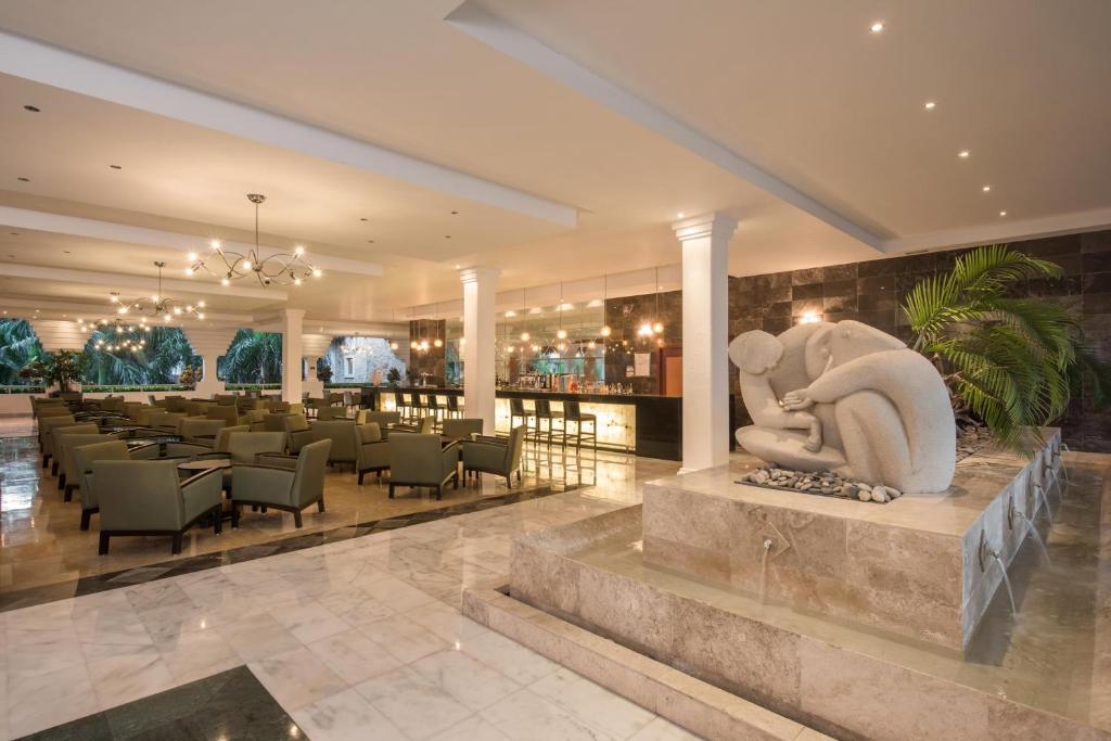 Mūsdienīgs viesnīcas interjers ar elegantu akmens skulptūru un zaļām mēbelēm, kas rada relaksējošu atmosfēru. Apgaismojums un viesmīlība izceļ šo telpu kā ideālu vietu atpūtai.