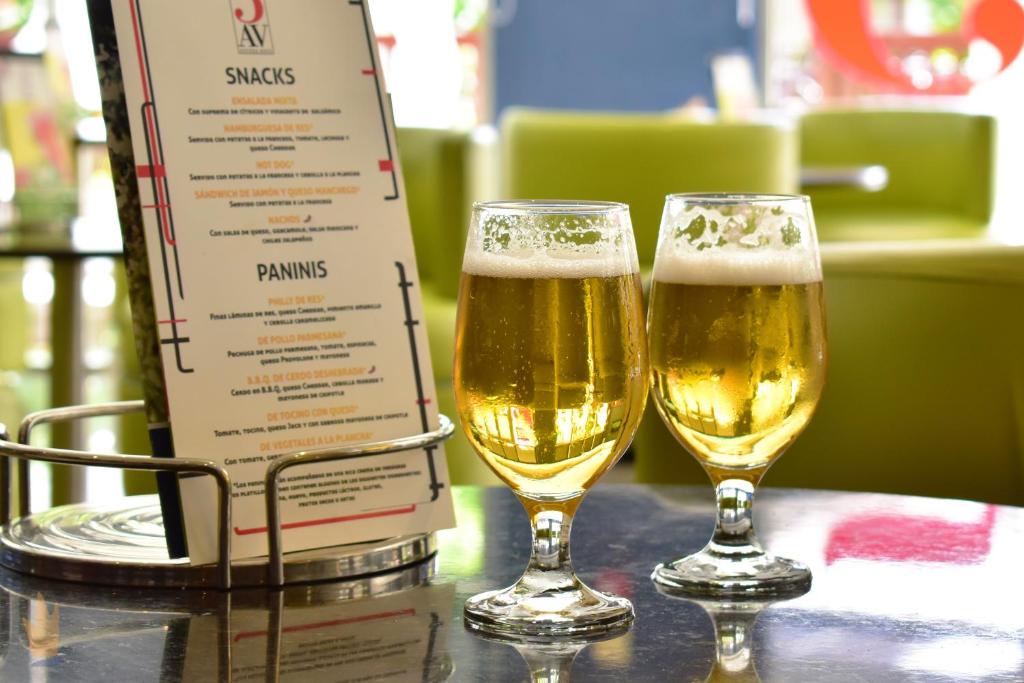 Divas glāzes ar dzidru alu uz galda, blakus ēdienkartes ar uzkodu un panīnu piedāvājumu. Gaisīga un viesmīlīga atmosfēra.