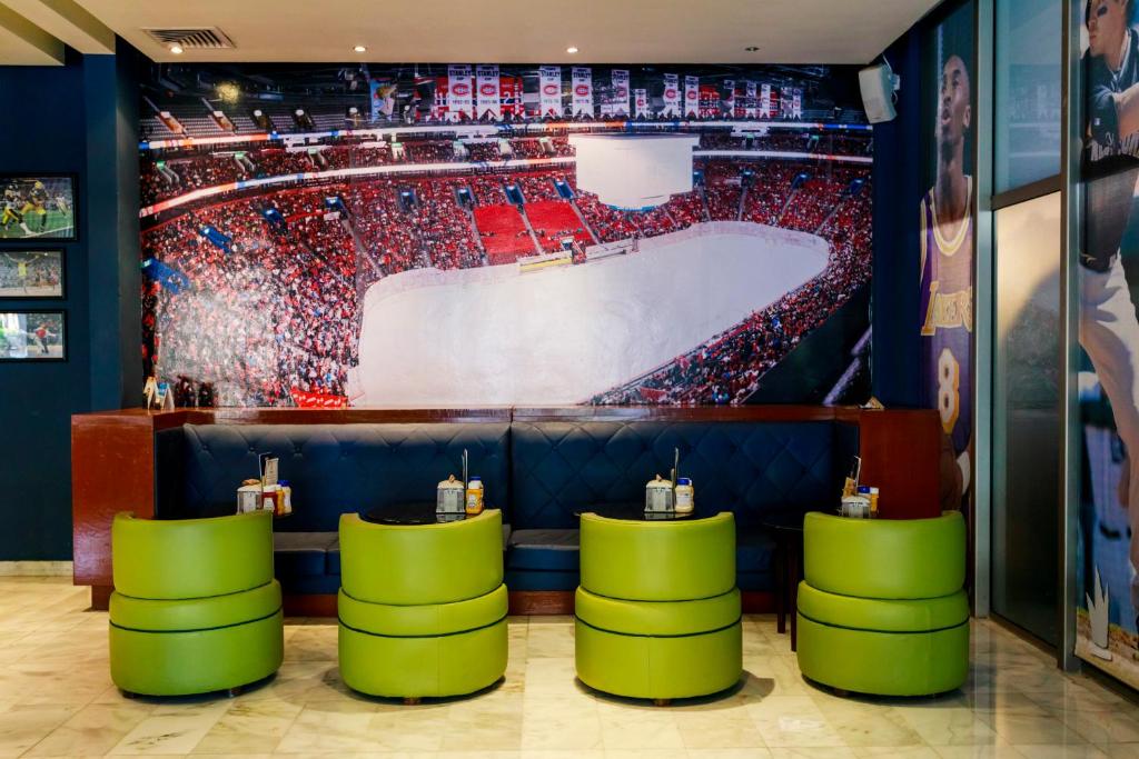 Sporta bārs ar modernu interjeru, kurā redzami zaļi krēsli un liela sporta pasākuma fotogrāfija uz sienas. Ideāla vieta, lai baudītu spēles un relaksētos ar draugiem.