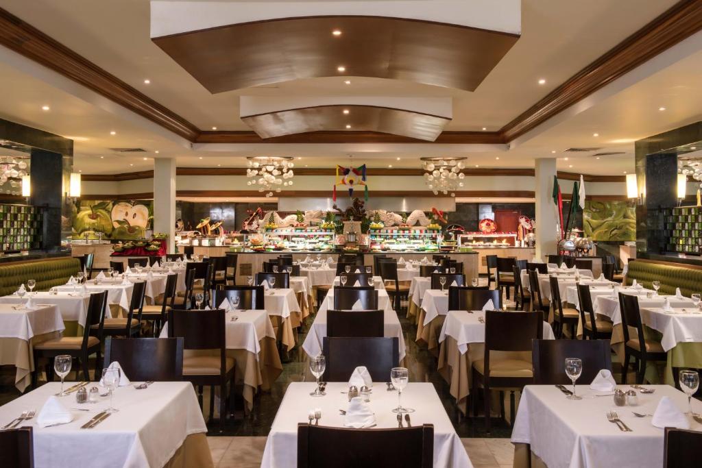 Elegants restorāns ar baltām galdautām un modernu interjeru, kas piedāvā plašu ēdienu izvēli bufetē. Gaismas un dekorācijas rada patīkamu atmosfēru.