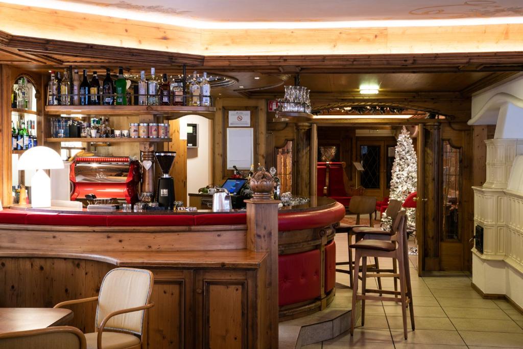 Elegants bārs ar koka apdari, sarkanu dīvānu un plašu dzērienu izvēli, kas radīs mājīgu atmosfēru. Aiz bāra redzama Ziemassvētku egle, piešķirot telpai svinīgu noskaņu.