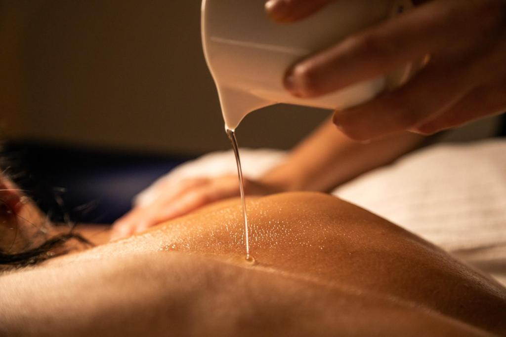 Masāžas sesija ar eļļas pilināšanu uz ādas, radot relaksējošu atmosfēru. Ideāli piemērota skaistumkopšanas un labsajūtas pakalpojumu reklamēšanai.