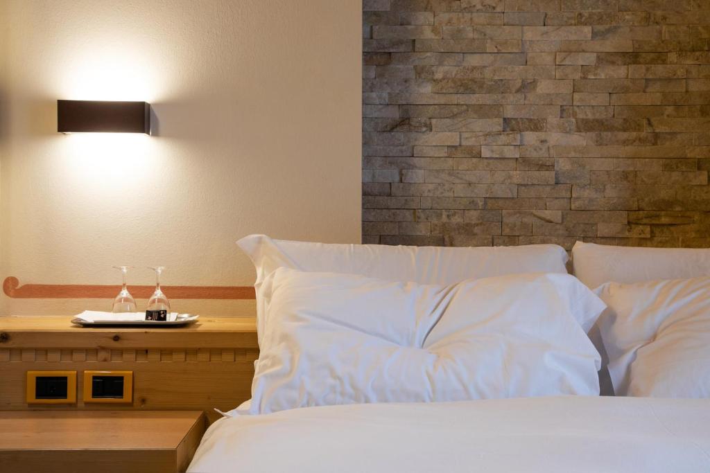 Mūsdienīgs guļamistabas interjers ar akmens sienu, gultu ar baltām spilveniem un galdiņu ar glāzēm.