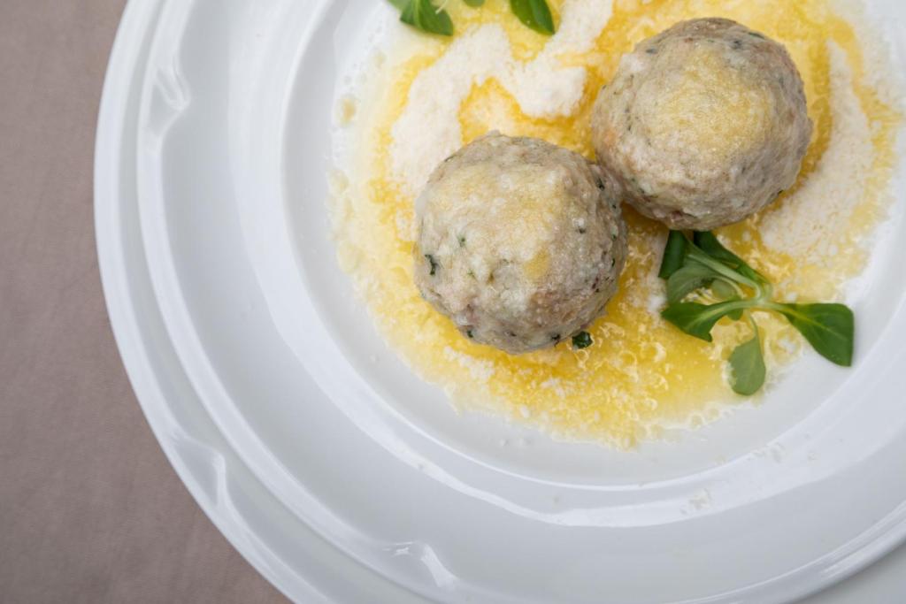 Divas gaļas bumbiņas ar šķidru sviestu un zaļumiem uz balta šķīvja.