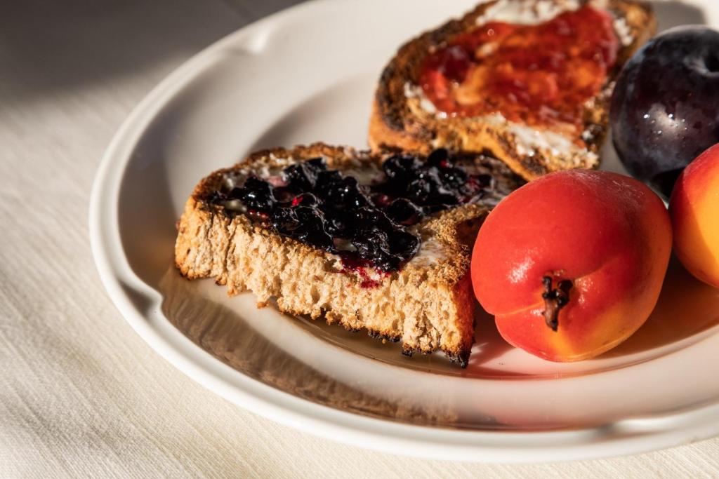 Svaigi grauzdiņi ar ievārījumu un augļiem uz baltā šķīvja, radot pievilcīgu un veselīgu brokastu kompozīciju.