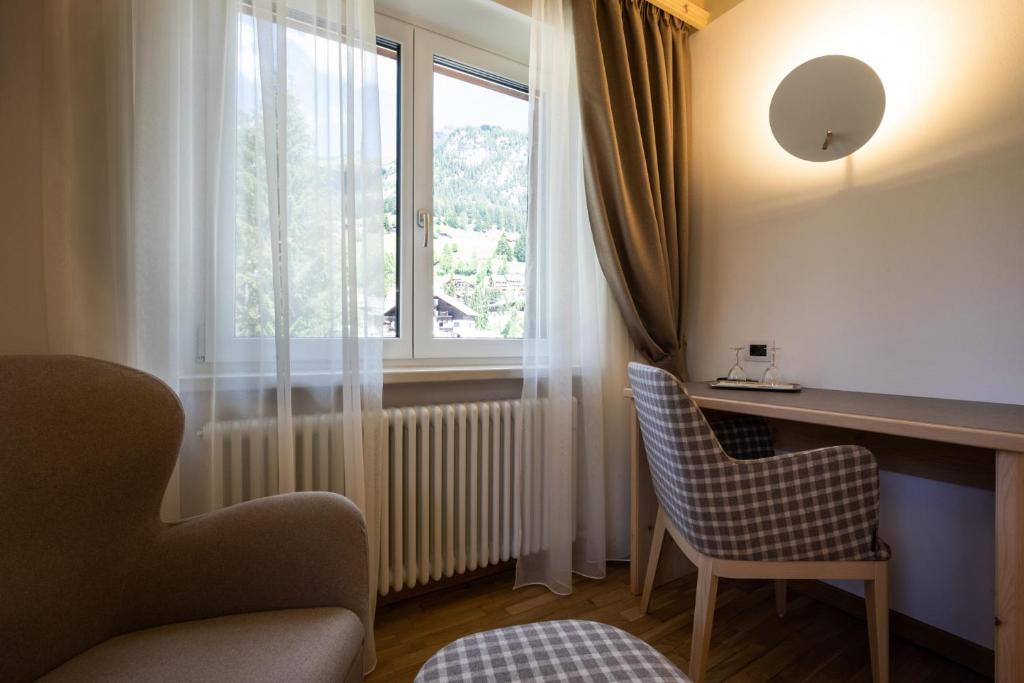 Mūsdienīgs viesnīcas numurs ar skatu uz kalniem, iekārtots ar ērtu krēslu un darba galdu. Gaismas un auduma elementi rada patīkamu atmosfēru.