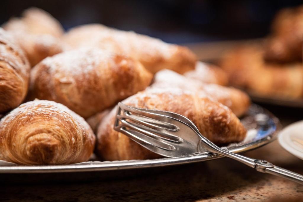 Svaigi cepti kruasāni uz sudraba paplātes, apkaisīti ar pūdercukuru, papildināti ar metāla dakšiņu.