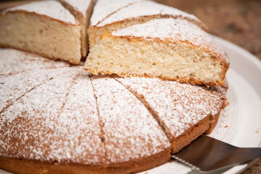 Gaisīgs un sulīgs kūka ar pūdercukuru, sagriezta šķēlēs, uz baltas šķīvja. Ideāla desertam vai svētku galdam.