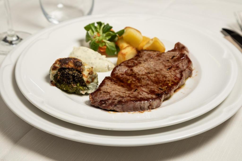 Garšīgs steiks ar ceptiem kartupeļiem un dārzeņu garnējumu, pasniegts eleganti uz baltā šķīvja.