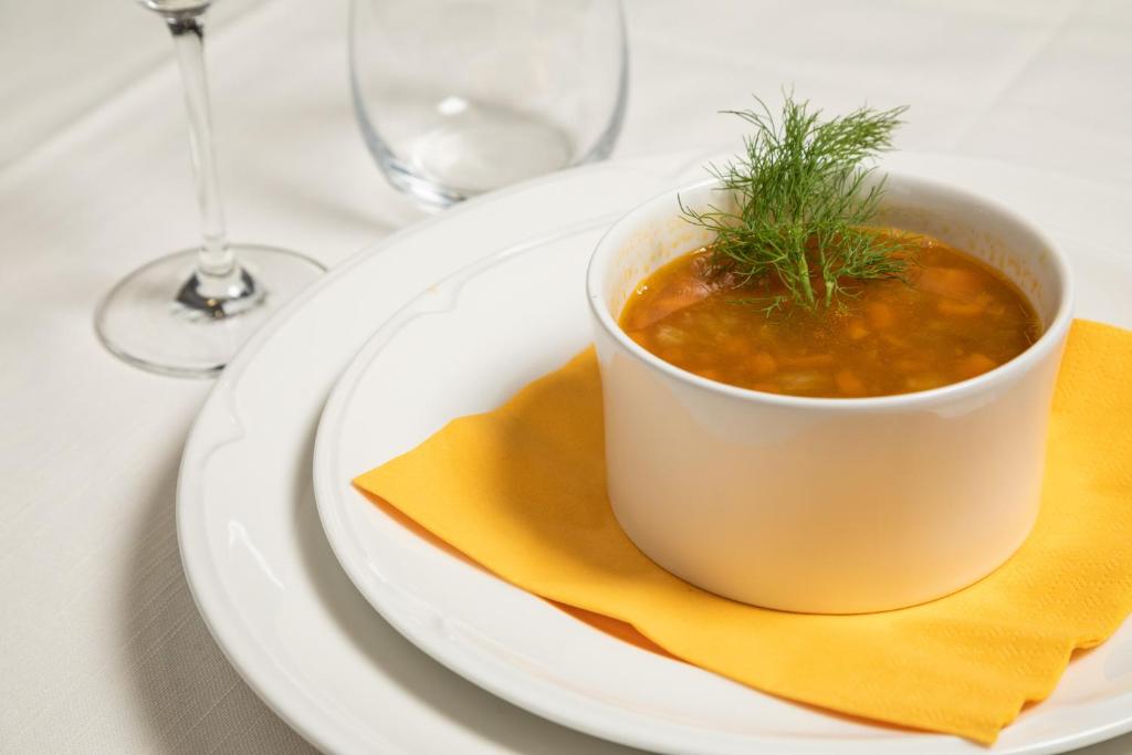 Siltā zupa pasniegta baltā traukā uz baltas šķīvja ar dzeltenu salveti, dekorēta ar dillēm. Ideāls ēdiens, lai izbaudītu siltu maltīti.