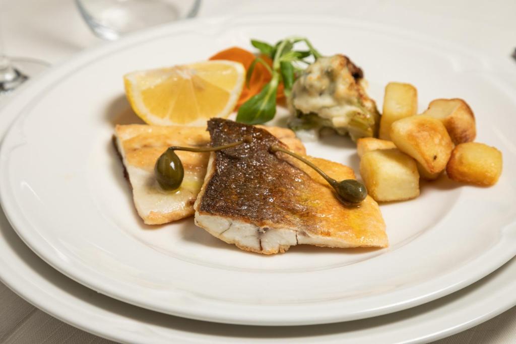 Garšīgas ceptas zivis ar citronu, kapariem un ceptiem kartupeļiem, pasniegtas ar salātu garnējumu.