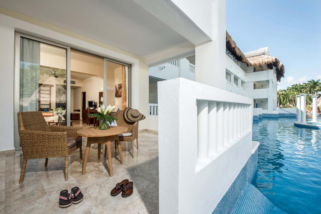 Mūsdienīga viesnīcas terase ar ērtām sēdvietām, galdu un ziedu kompozīciju, kas atrodas blakus baseinam. Svaiga atmosfēra un relaksējošs skats uz dabu.