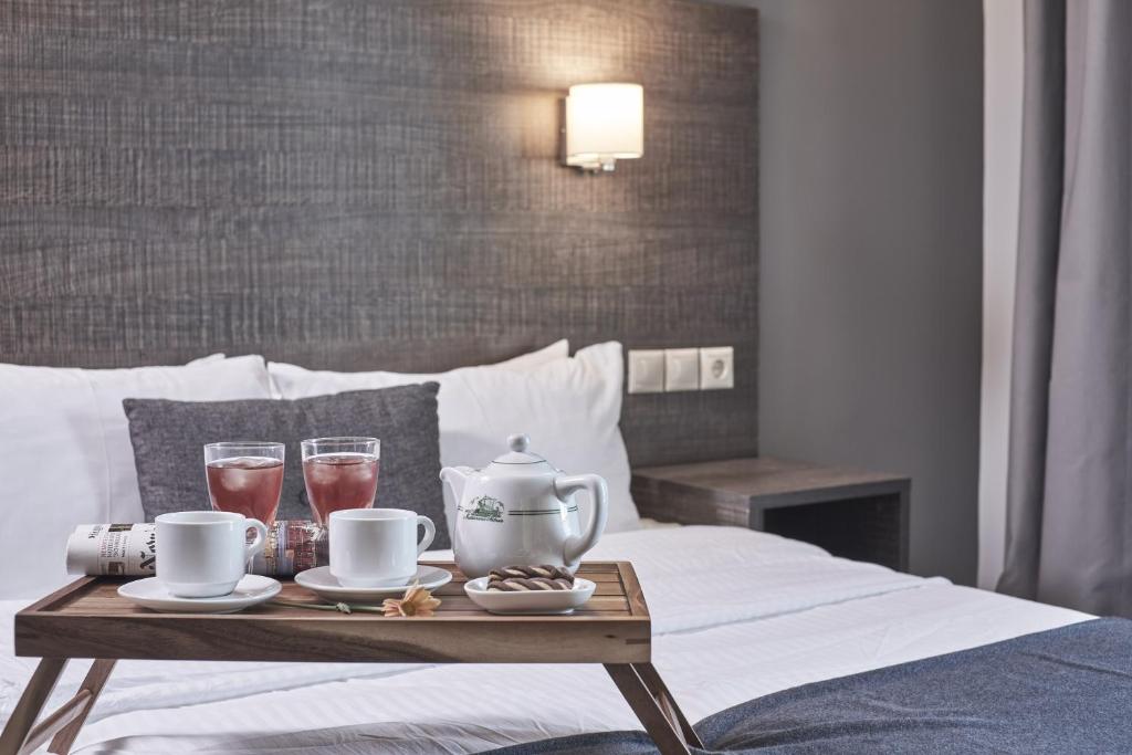 Gultas galda ar divām glāzēm dzēriena, tējkannu un kafijas tasītēm, dekorēta ar ziedu; mūsdienīga viesnīcas istaba.