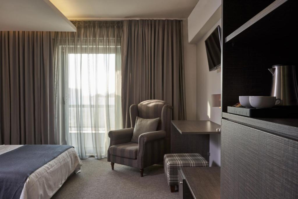 Mūsdienīgs viesnīcas numurs ar ērtu atpūtas krēslu, galdu un televizoru. Lielas logu aizkari nodrošina dabisko apgaismojumu un mājīguma sajūtu.