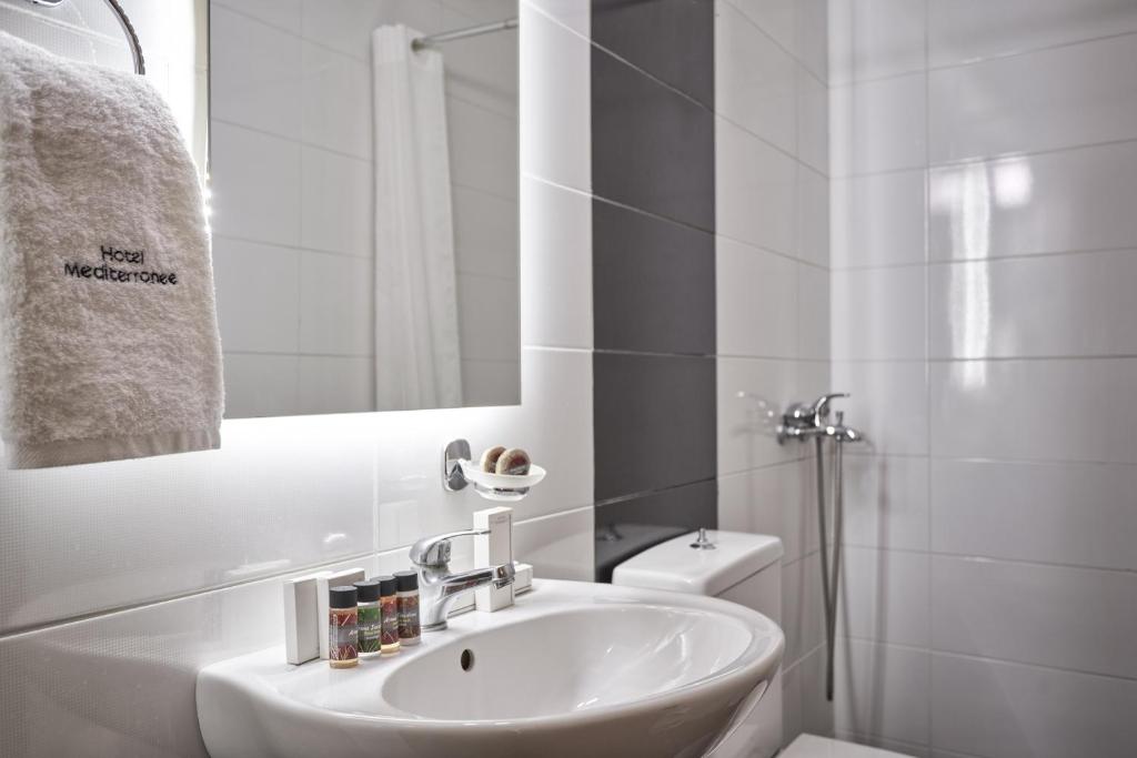 Mūsdienīga viesnīcas vannas istaba ar baltiem flīzēm, spoguli un higiēnas piederumiem. Pievērsta uzmanība detaļām un tīrībai.