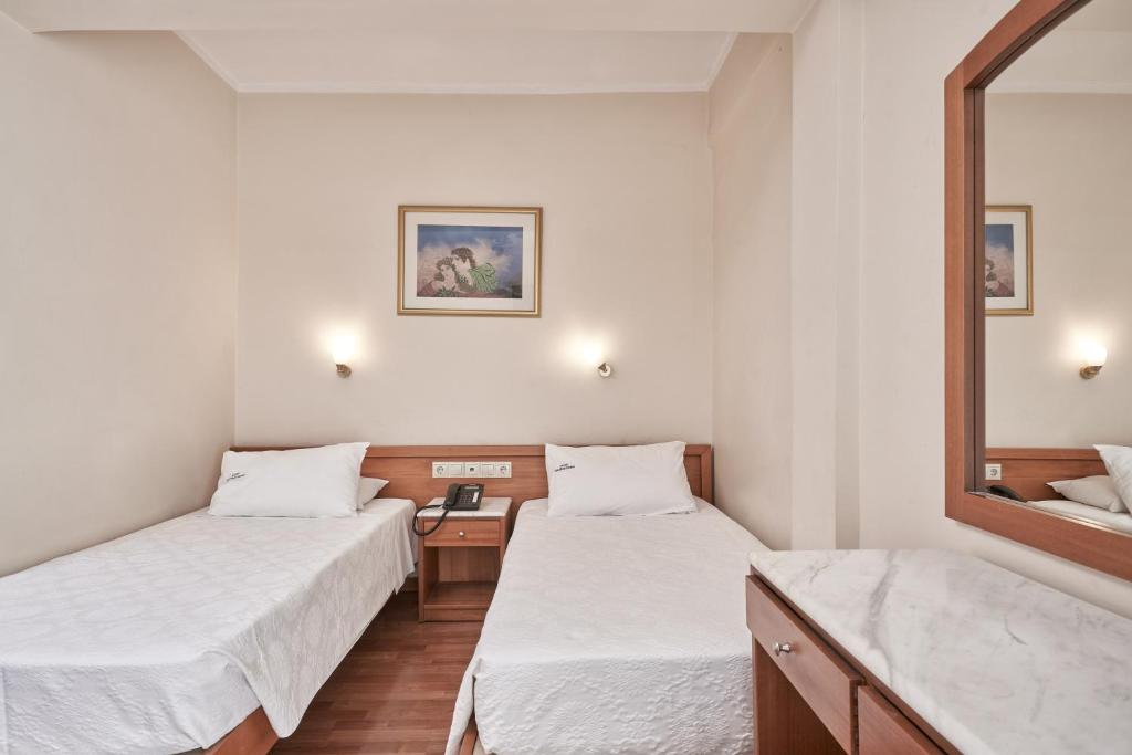 Divvietīga guļamistaba ar divām atsevišķām gultām, koka mēbelēm un gaismas avotiem. Sienā ir attēls, kas piešķir telpai mājīgumu.